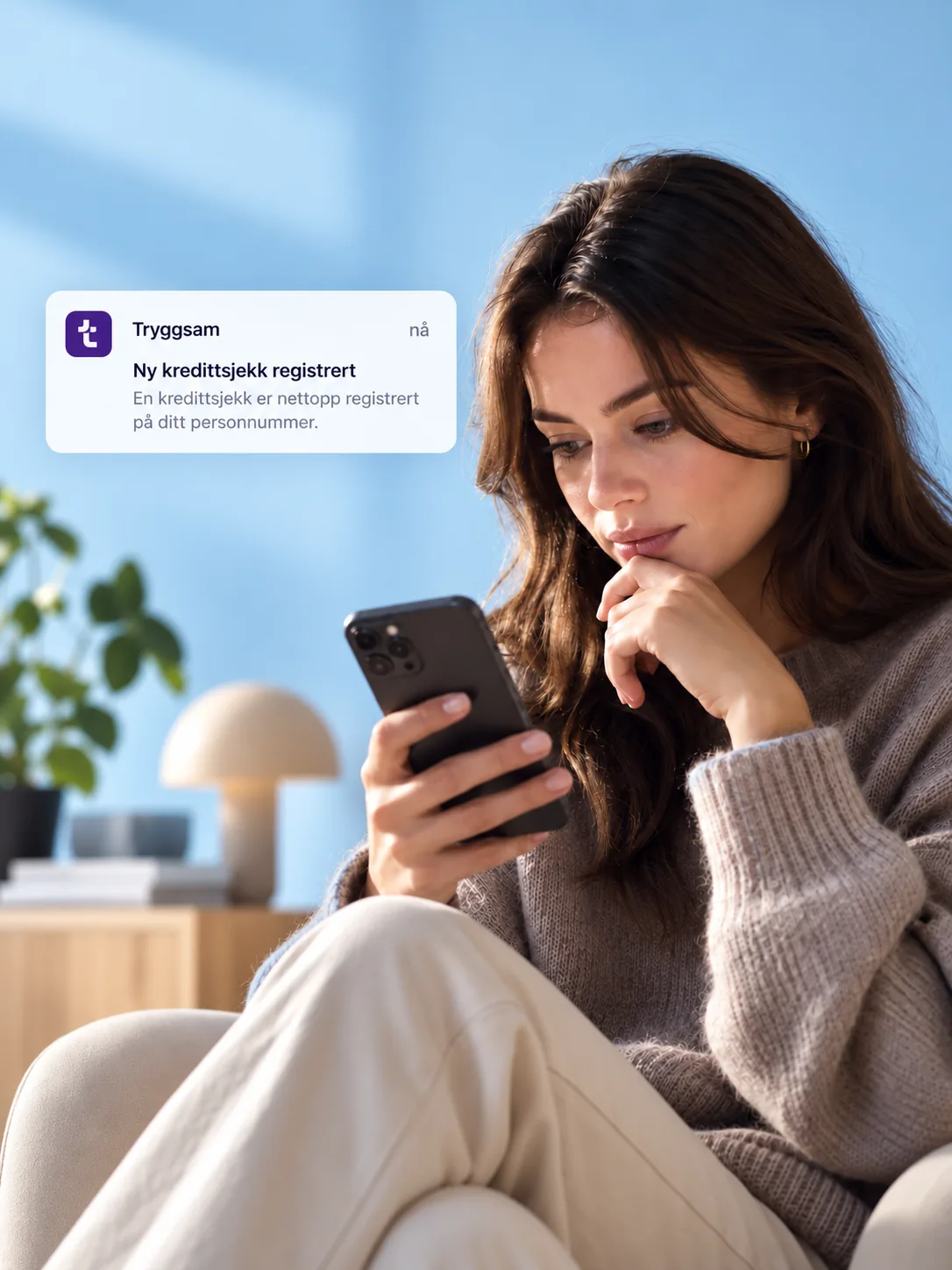 Kvinne i sofa ser på mobilen med varsel om ny kredittsjekk